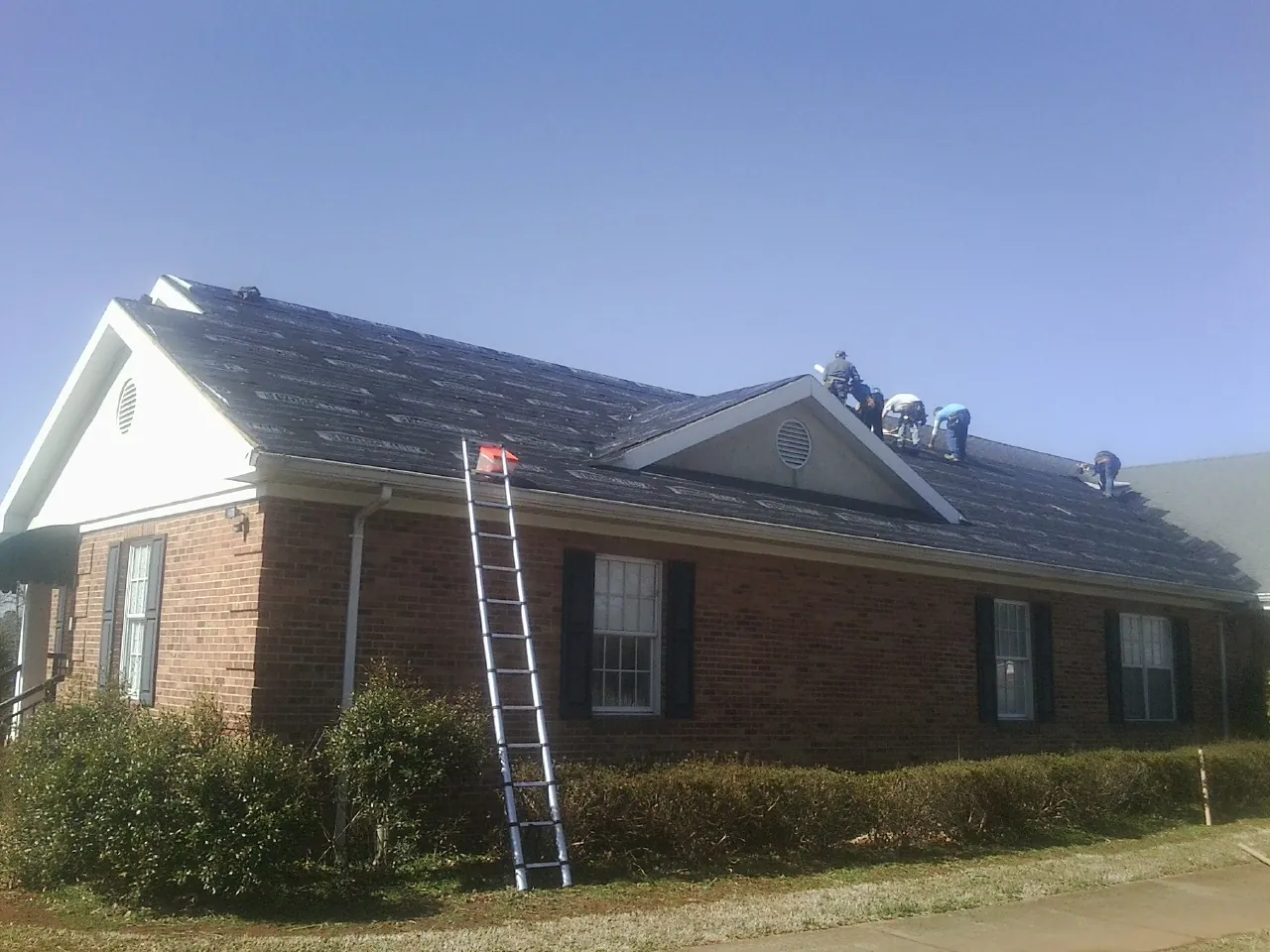 Crew tearing shingles off a brick ranch roof with a ladder set — Metal Roof Repair work by our crew in Sugar City