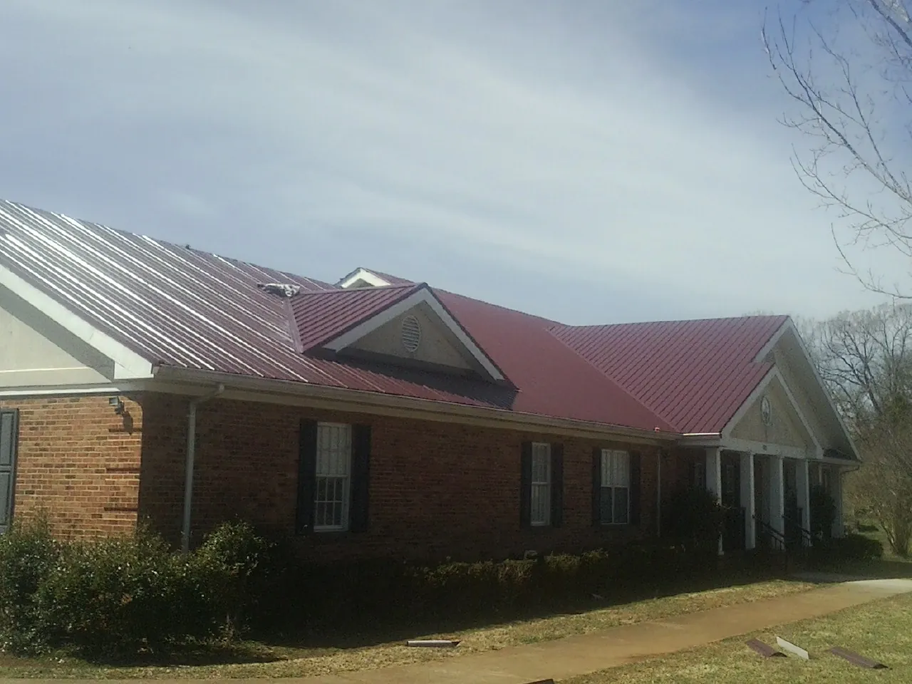 Red metal roof with gabled entries on a long brick building, from a Hail Damage Roof Repair job in Sugar City