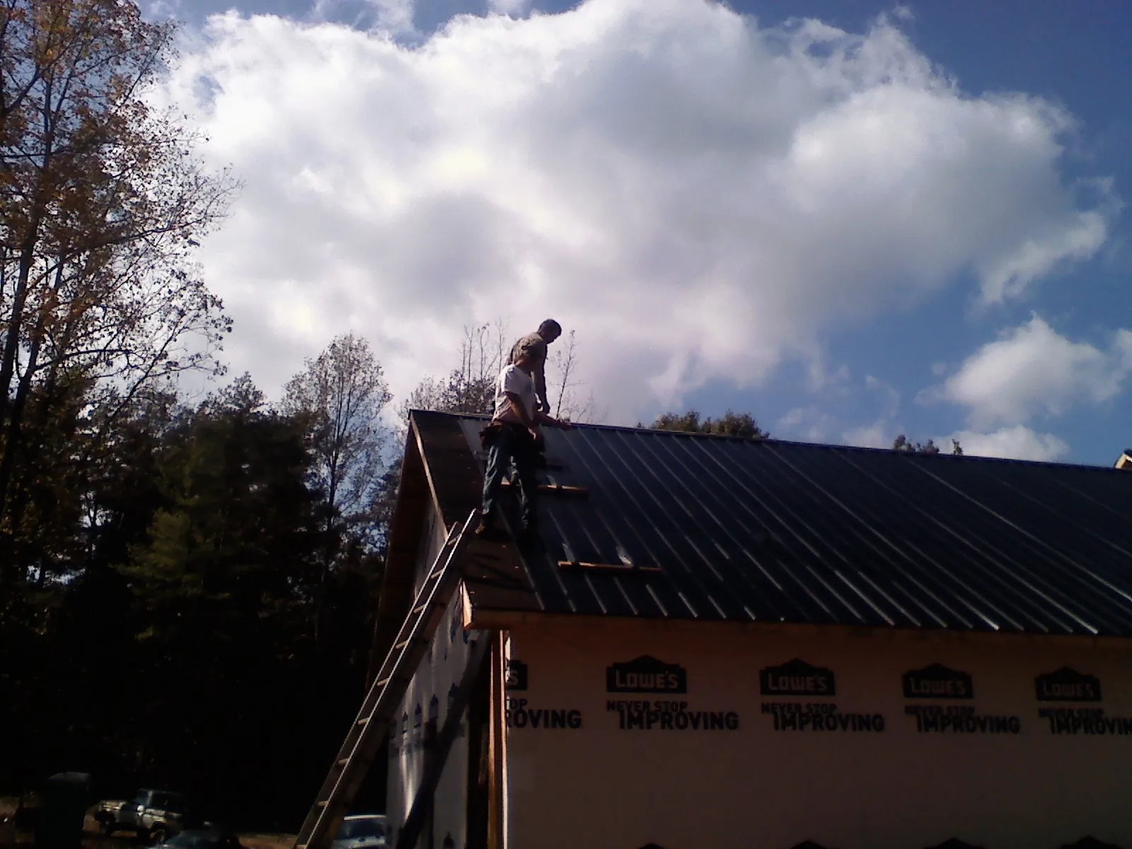 Roofer fastening dark metal panels high against a cloudy sky, from a Roof Inspection job in Sugar City