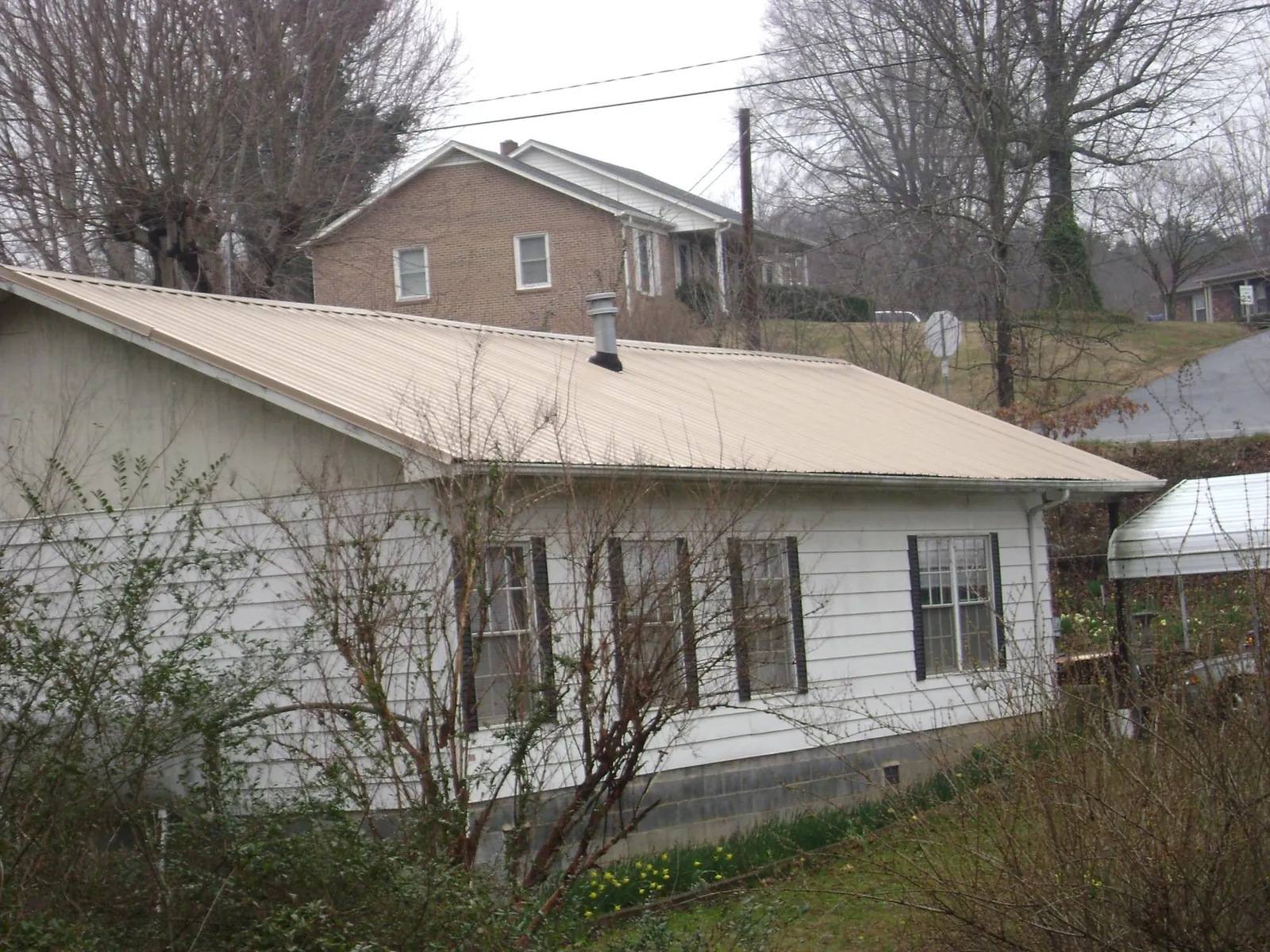 Tan metal roof on a white sided house set into a hillside — Commercial Roofing by Roofing Brothers in Sugar City